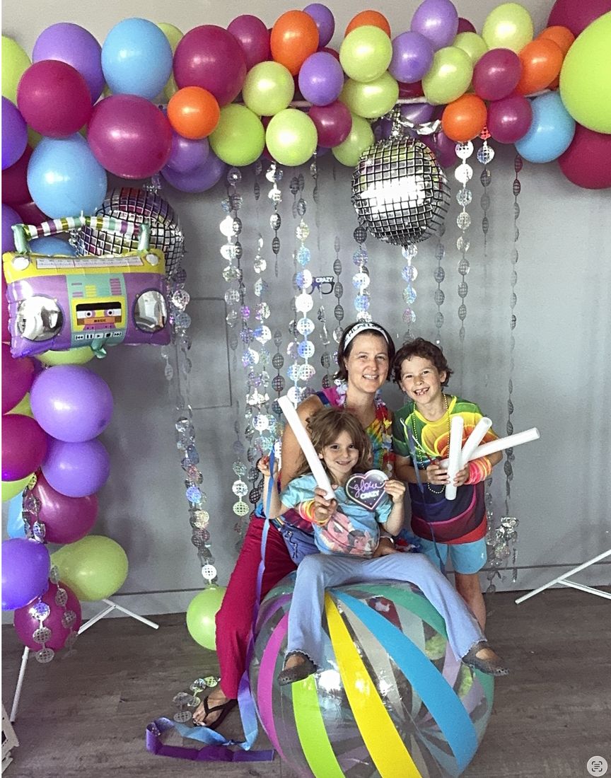 A mom and two kids with glow sticks and a giant beach ball